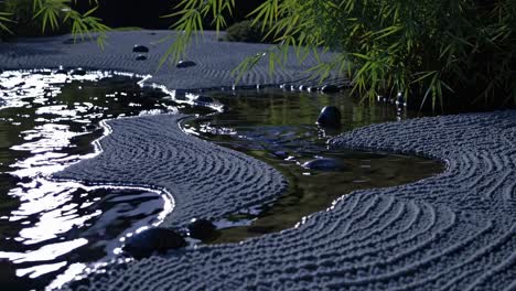 gentle water streaming across meticulously arranged zen garden, creating serene landscape with bamboo leaves cascading near dark stones under soft illumination