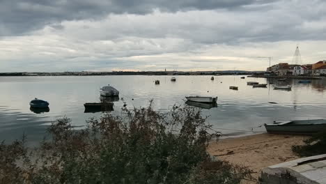 boats moored at an urban beach in portugal on a cloudy sunset - dolly shot