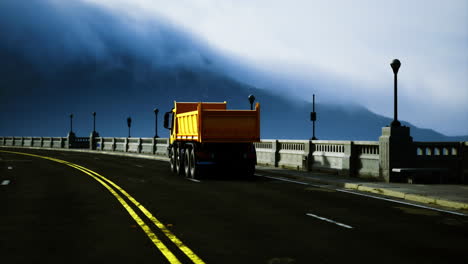 bright yellow truck drives along a quiet road near the mountains at dusk