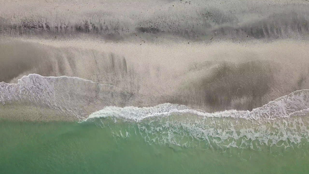 Top down shot, birds eye, of couple sitting on beach reading, pushes to reveal waves crashing on shore.