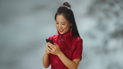 asian young cheerful woman in red traditional clothes texting cheerfully on mobile phone