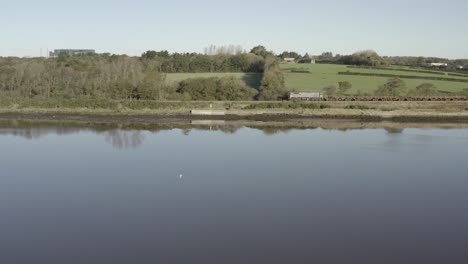 low flight over glassy river to freight train passing green farmland