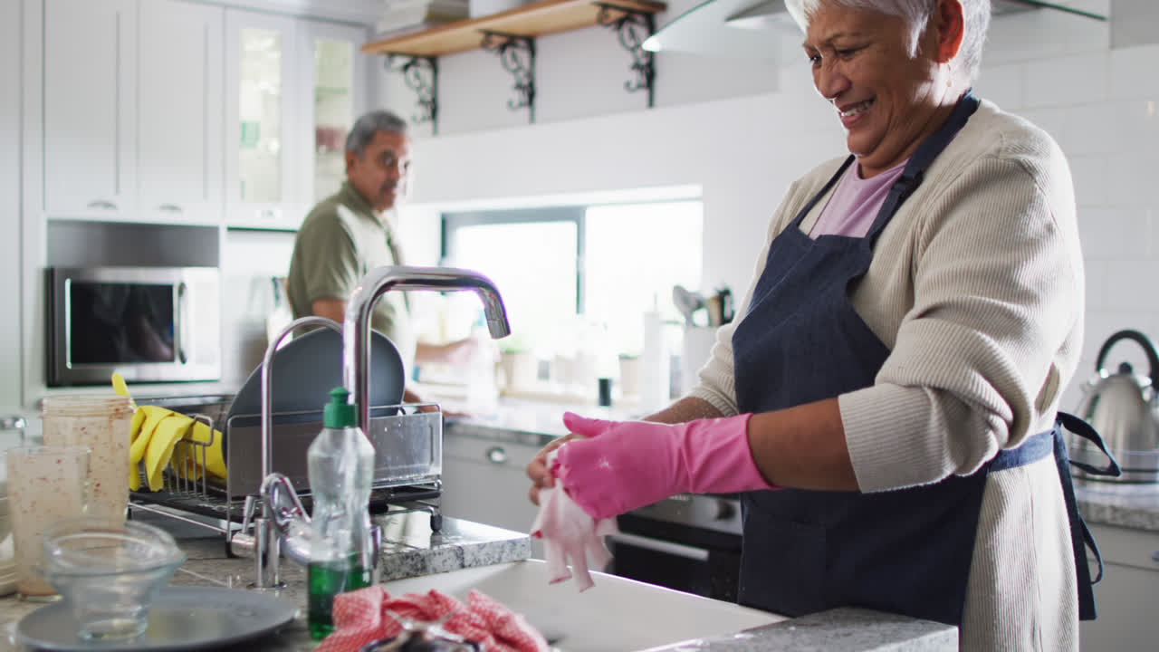 una pareja bi-racial feliz lavando platos en la cocina
