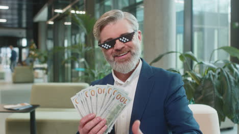 rich mature businessman putting on thug life sunglasses showing money dollar in modern office lobby