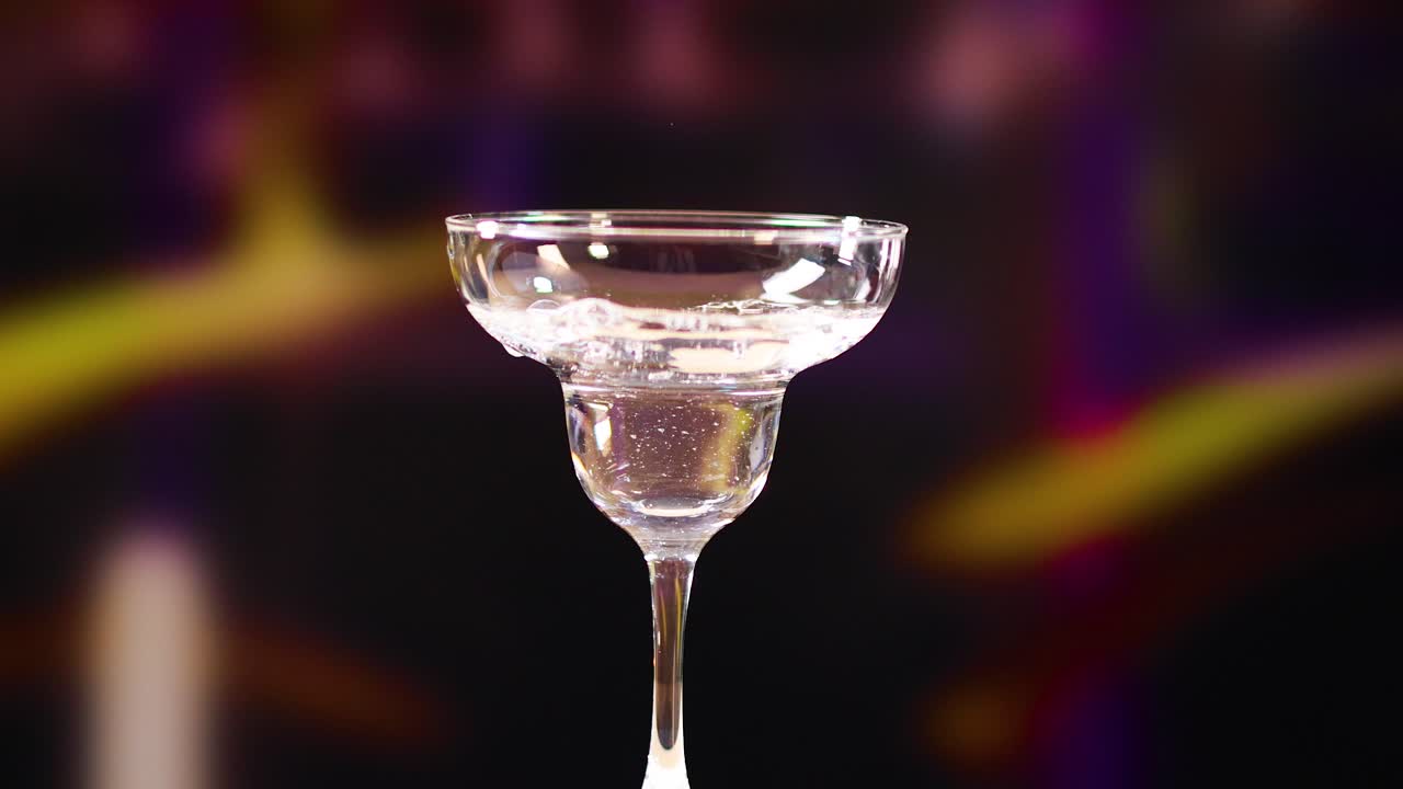 un vaso de martini está lleno de líquido y adornado con aceitunas contra un fondo borroso