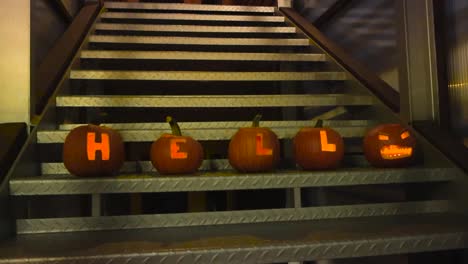 halloween carved pumpkins on a gray metal staircase spelling out hell and with a spooky face decorations during night time in october