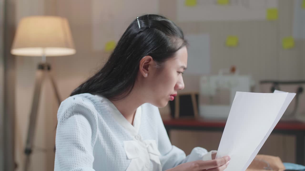 화가 난 아시아 여성 가방 디자이너가 사무실에서 레이아웃을 보면서 머리를 긍정적으로 흔들고 있습니다.