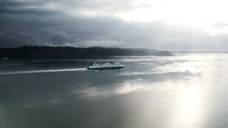 commuter ferry cruises along dark water reflecting streaming sunlight and gloomy clouds, aerial