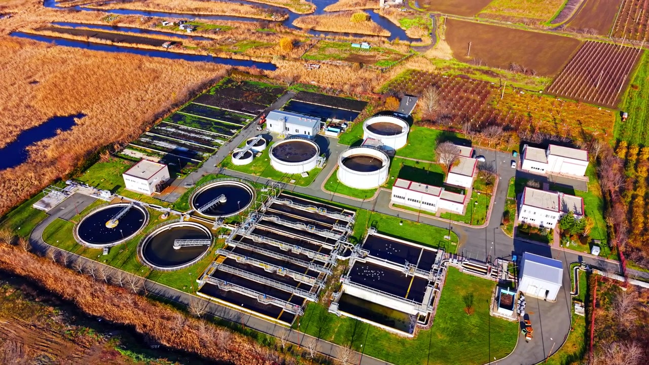Drone perspective of industrial sewage purification facility surrounded by rural wetlands and agricultural fields. Aerial view of wastewater treatment plant.