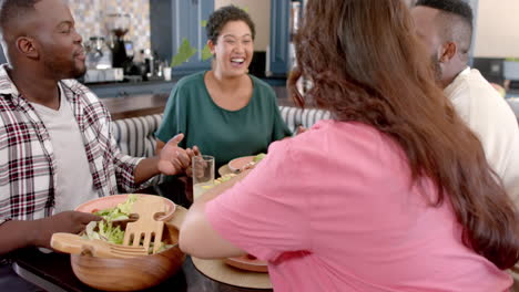 diverse friends laughing and enjoying meal together at home dining table