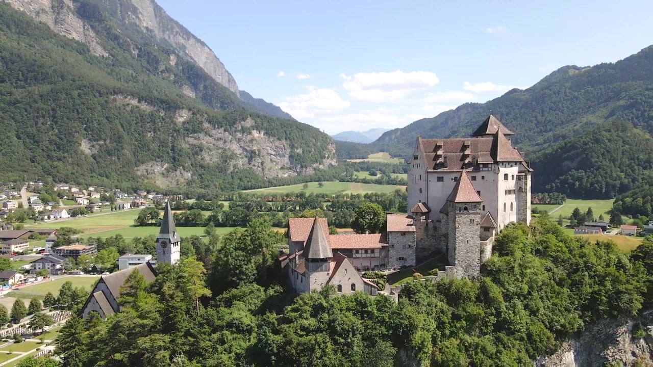 Gutenbergin linna Burg Gutenbergissa, josta avautuu näkymä Balzersin kaupunkiin Liechtensteinissa, vuorten ja vehreyden ympäröimänä kirkkaana aurinkoisena päivänä, dronekuva etääntyy