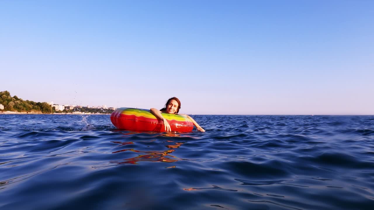 A woman swims in an inflatable bright life buoy in the blue sea enjoying the summer sun. Sea relaxation.
