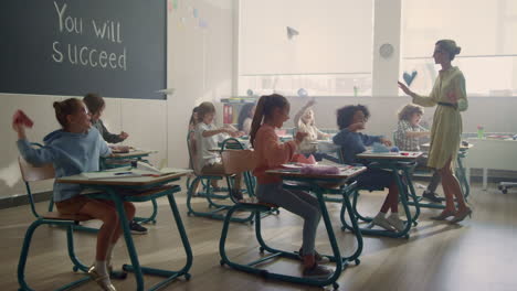 students sitting at desks in classroom. pupils playing with paper planes