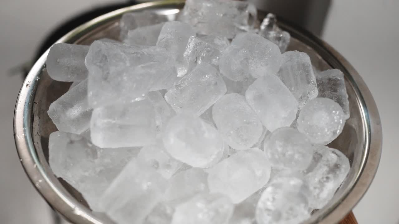 Primer plano de cubitos de hielo congelados llenando un cuenco de metal