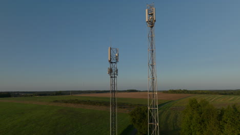 two radio towers in the middle of farmland during sunrise, aerial orbital dolly in tilting upward