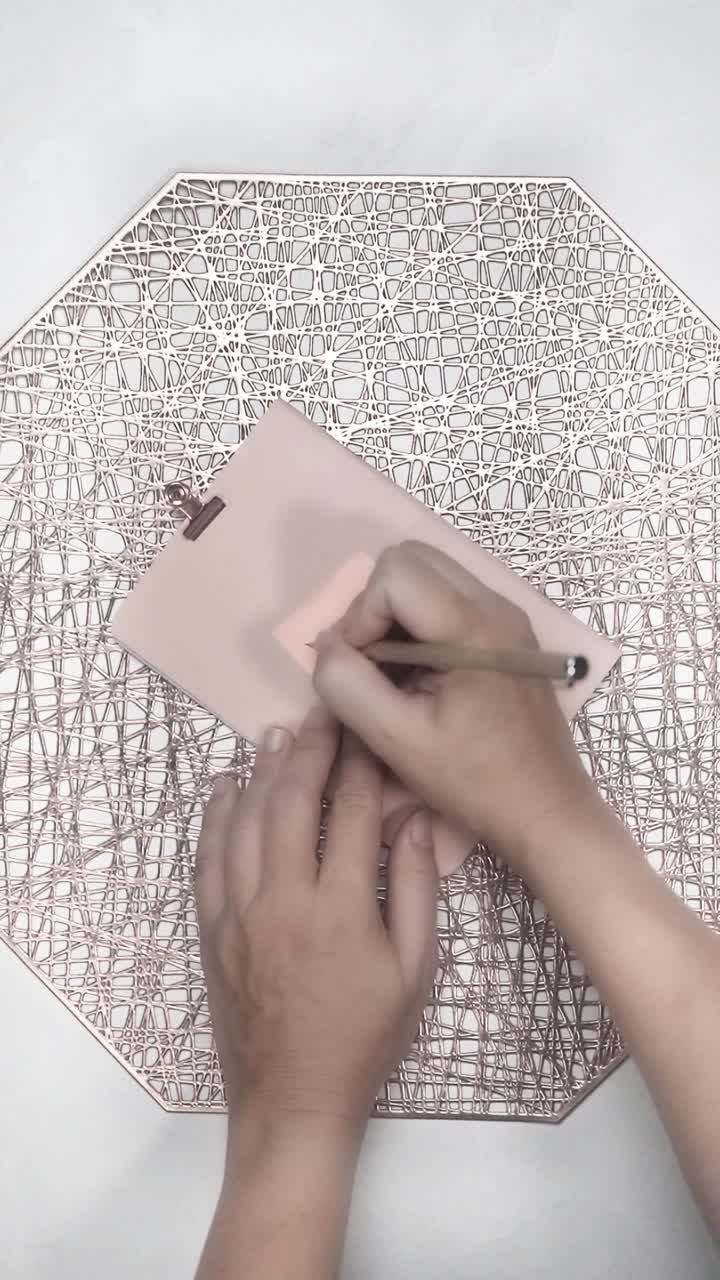 Hands Writing a Reminder on a Pink Sticky Note