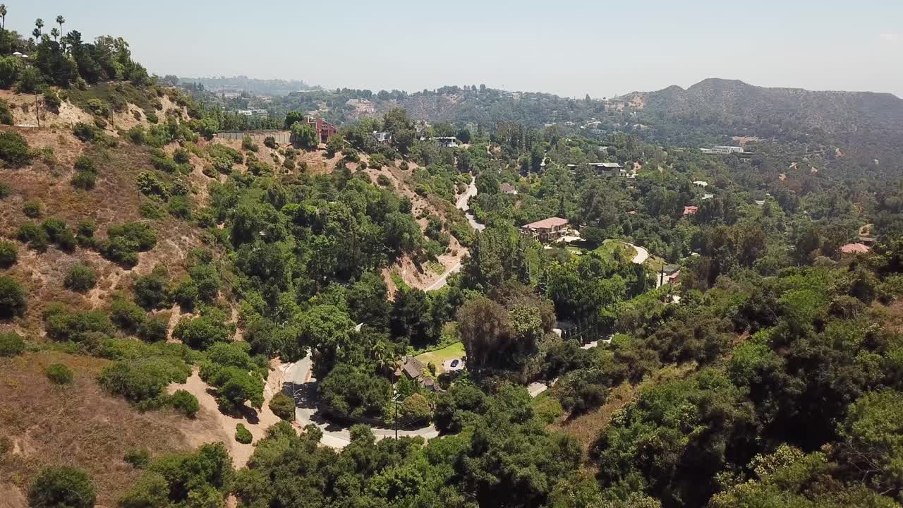 vuelo aéreo sobre montañas con calles y villas en beverly hills durante un día soleado