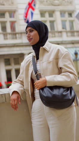 vertical video portrait of smiling muslim businesswoman wearing hijab and modern business suit standing outside city office buildings 3