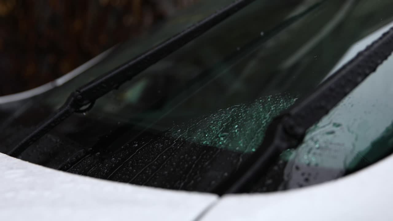 A video of a car's windshield wipers moving rain droplets out of the way during a rain shower.