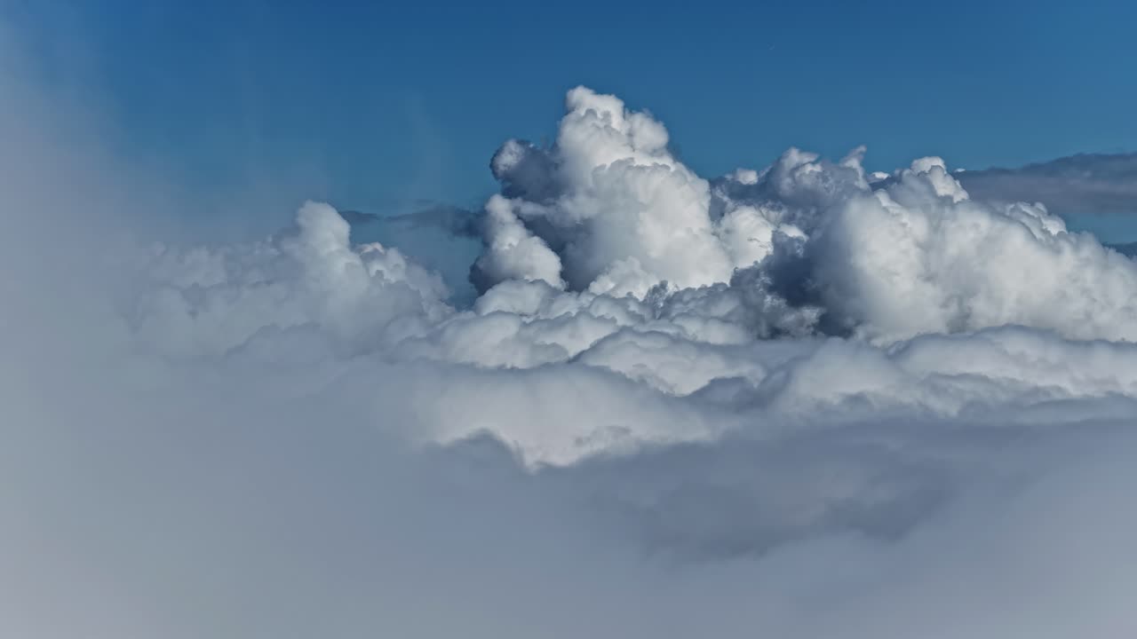 Towering cumulus clouds seen above the cloud layer against clear blue sky, aerial view