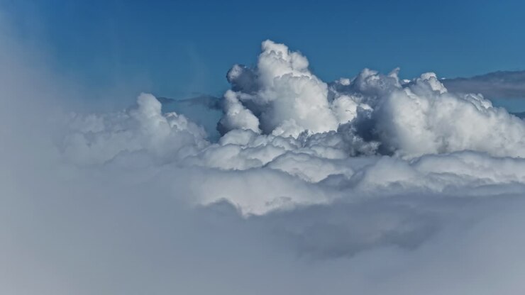 Towering cumulus clouds seen above the cloud layer against clear blue sky, aerial view
