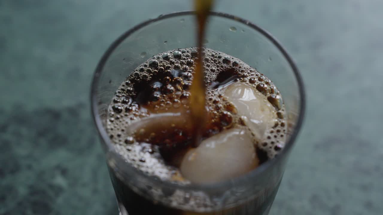 A close-up footage of pouring iced tea into a glass cup with ice cubes, with a blurred background