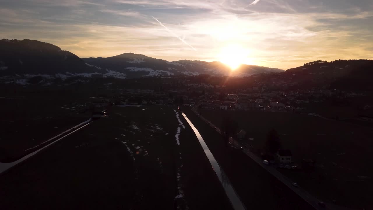 hermoso vuelo aéreo sobre una carretera y un pueblo mientras se pone el sol en suiza