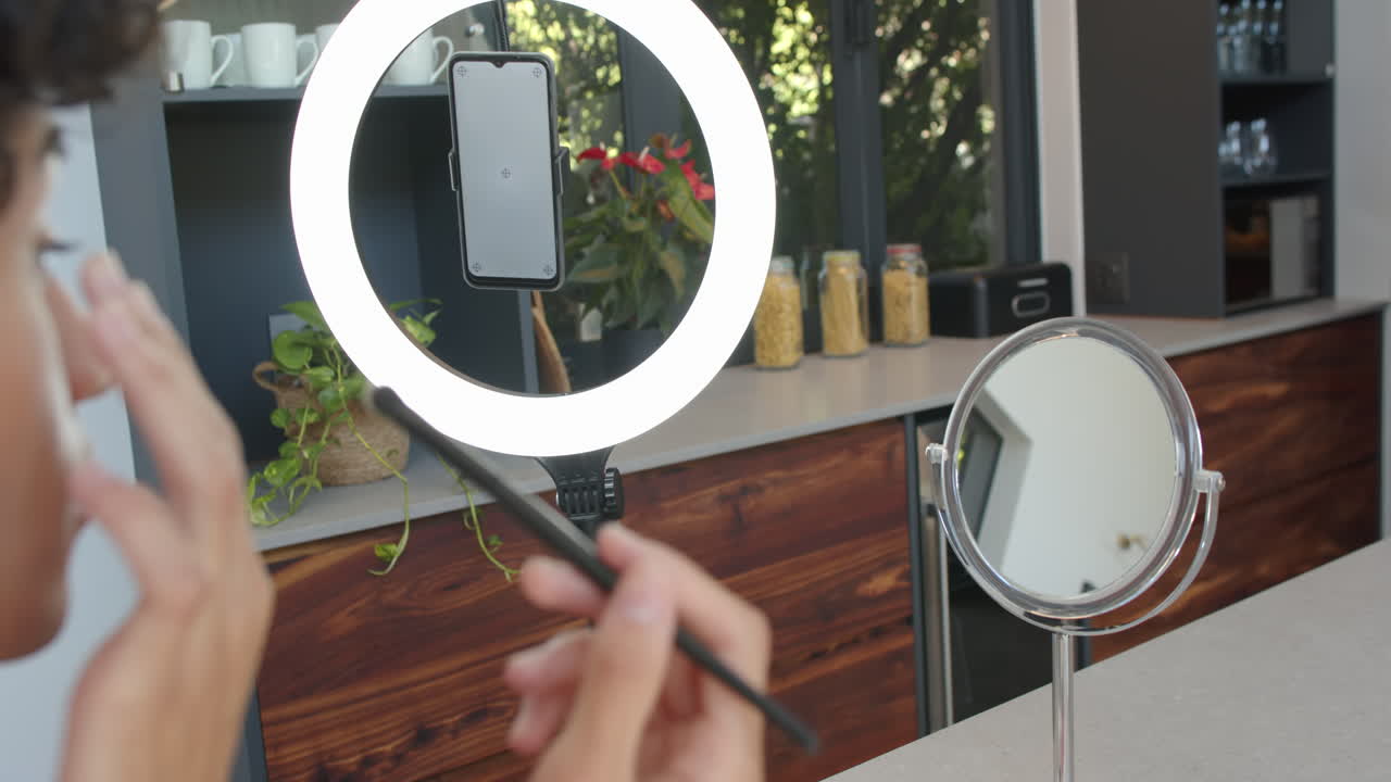 Applying makeup, person using smartphone with ring light in modern kitchen