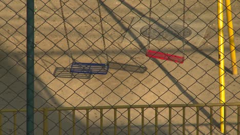 empty playground swings seen through a chain link fence