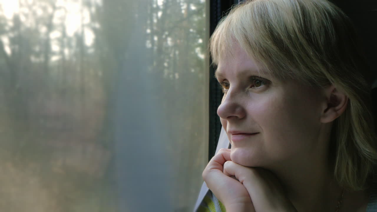Porträt einer jungen Frau, die im Zug reist und aus dem Fenster blickt. Die Sonnenstrahlen beleuchten sie.