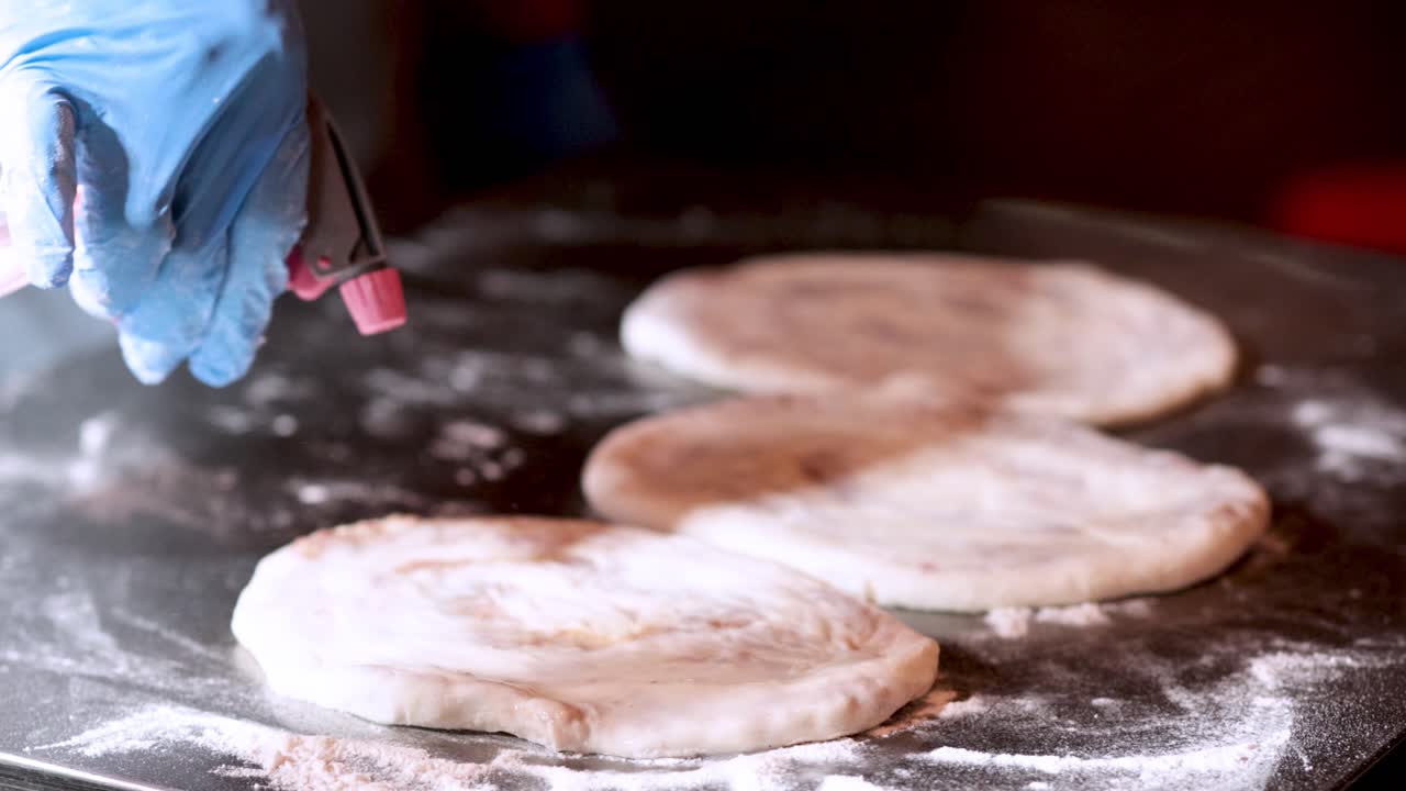 manos con guantes rociando la masa con una botella de agua
