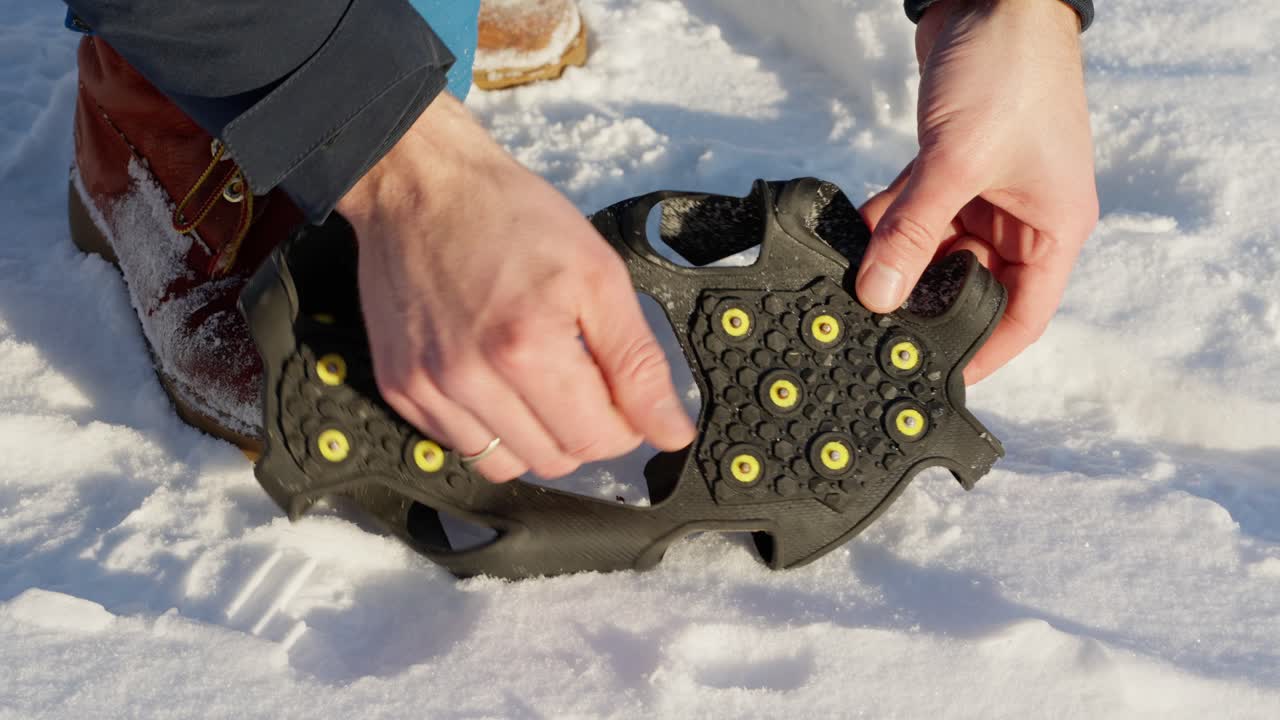 Man inspects spikes on bottom of rubber ice cleats, considers putting on boots, picks up spikes and walks away.