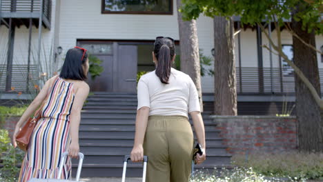 happy asian female friends with suitcases walking towards home on sunny day, slow motion