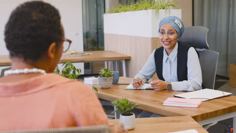 moslim zakenvrouw die aantekeningen maakt zittend op de tafel terwijl ze met haar zakenpartner praat