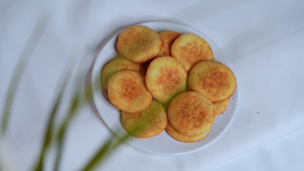 A female hand with colorful nails picks a golden Arabic cookie from a plate. High-resolution 4K footage ideal for food, culture, bakery, and lifestyle themes.