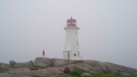 young woman walking with a lighthouse in the fog on an overcast day in nova scotia, canada peggy cove