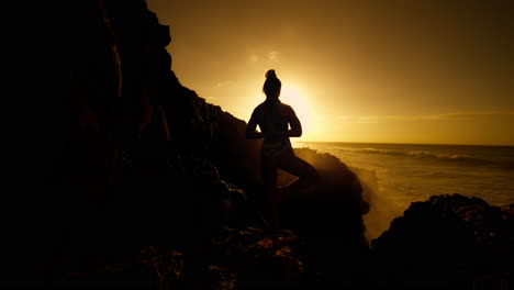 woman in yoga pose at sunset over the ocean