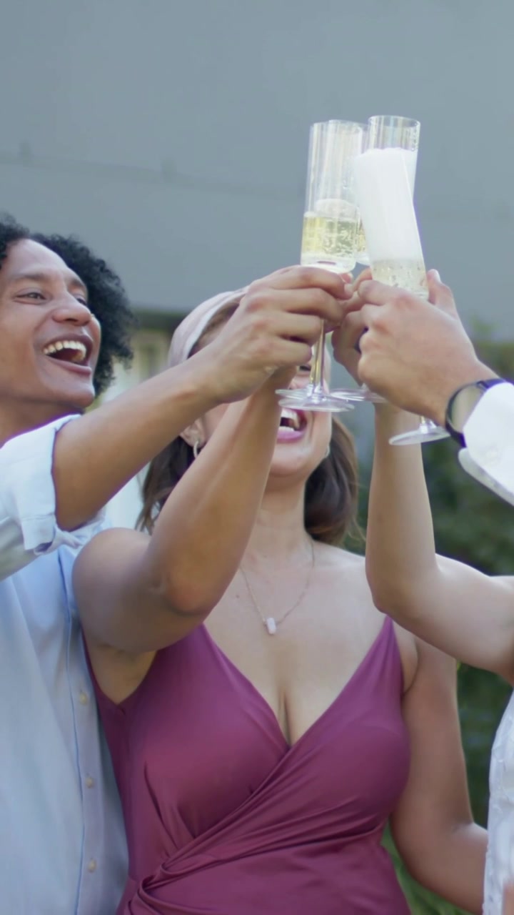 Vertical video: Signaling woman in mauve dress leading guests clinking flutes in yard marking vows