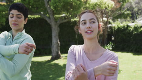una feliz pareja de lesbianas caucásicas estirándose en un jardín soleado, en cámara lenta