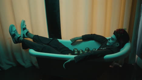 vista lateral de un joven durmiendo en una bañera con bolas de oro sobre él.