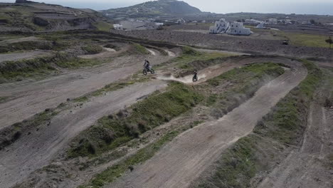 Drone-shot-pushing-forwards-as-two-motocross-riders-hit-jump-on-track