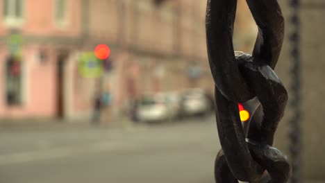 Street-urban-blurry-background-with-a-chain-in-the-foreground,-real-life-traffic,-vehicles-and-people-passing