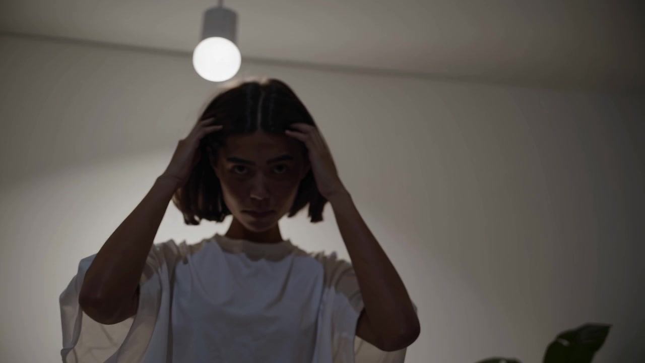 Stressed Young Woman Holding Her Head in Dimly Lit Room