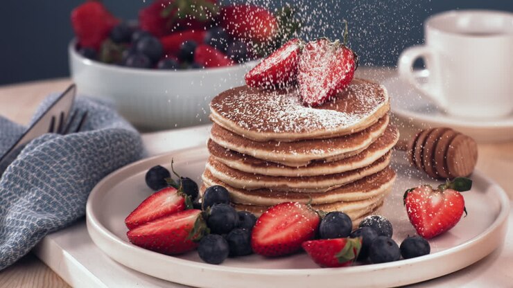 SUPER SLOW MOTION Powdered sugar is being sprinkled over the pancakes pile, served with blueberries and strawberries. Healthy tasty traditional breakfast. Shot with high speed cinema camera