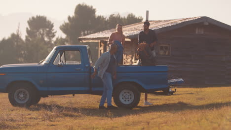 Gruppe-Von-Freunden-Entlädt-Rucksäcke-Vom-Pick-up-Truck-Auf-Dem-Roadtrip-Zu-Einer-Hütte-Auf-Dem-Land