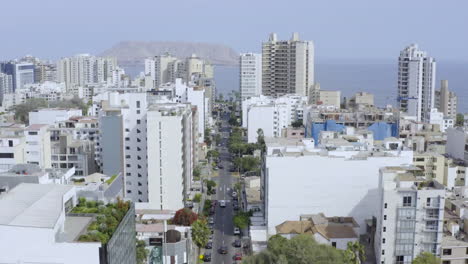 Drone-tracking-plane-over-the-city-of-Lima,-Peru-reaching-the-sea-on-the-green-coast