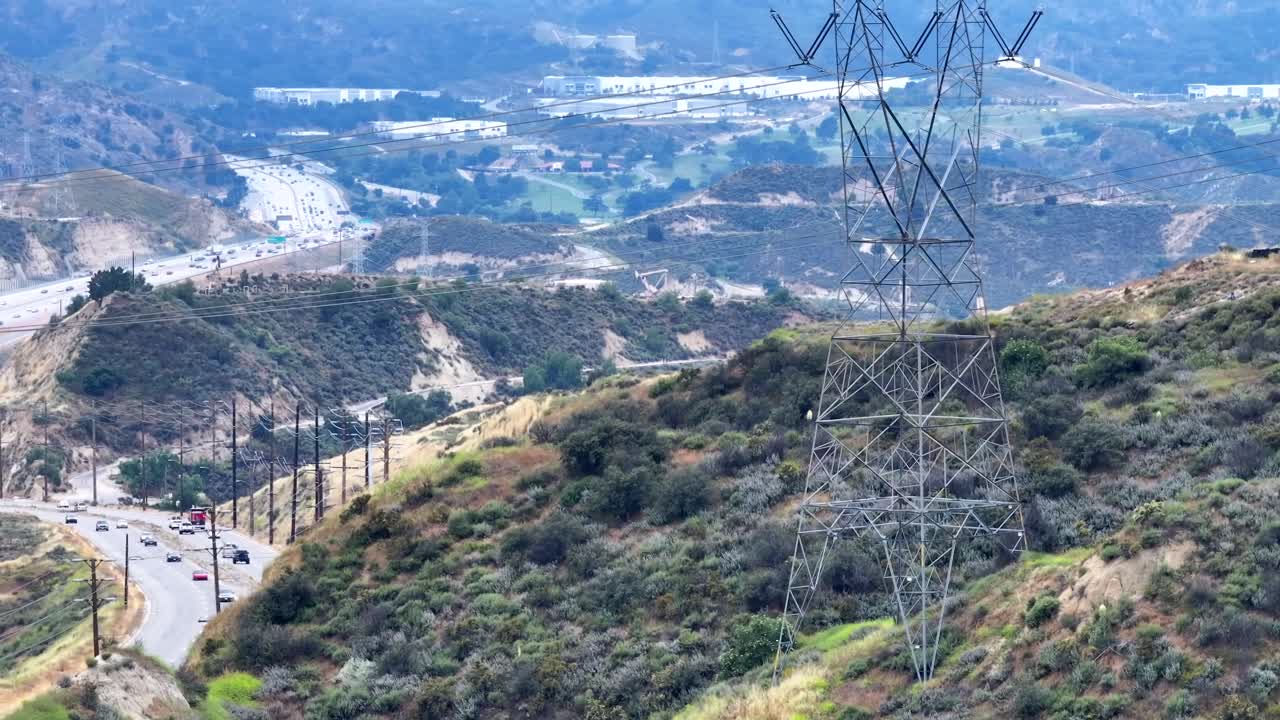 vista aérea que se eleva el pilar de energía eléctrica que se extiende a través del tráfico que viaja por la sinuosa carretera del valle en la distancia