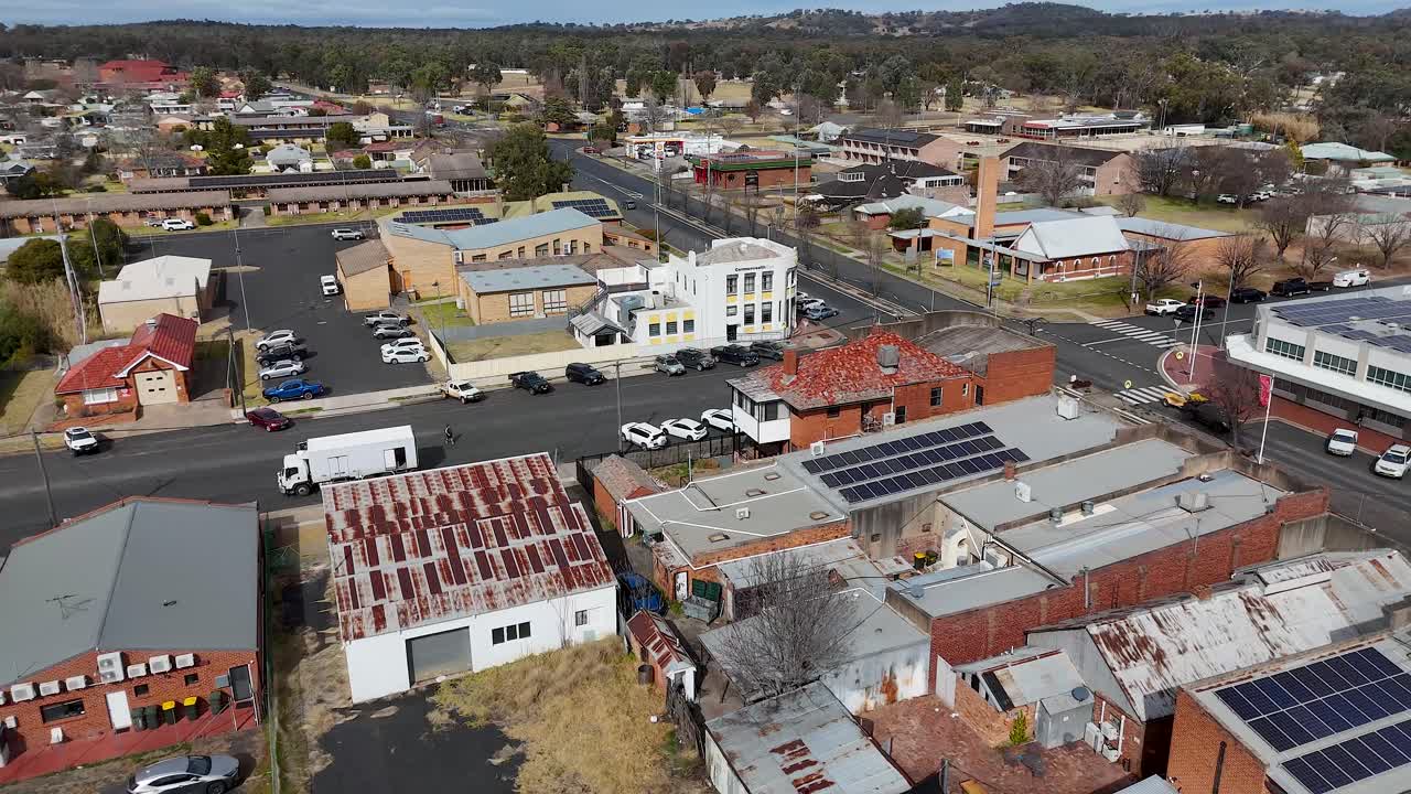 Aerial drone footage glides above a small Australian town’s main street, highlighting solar panels, commercial buildings, light traffic, and clear daylight conditions