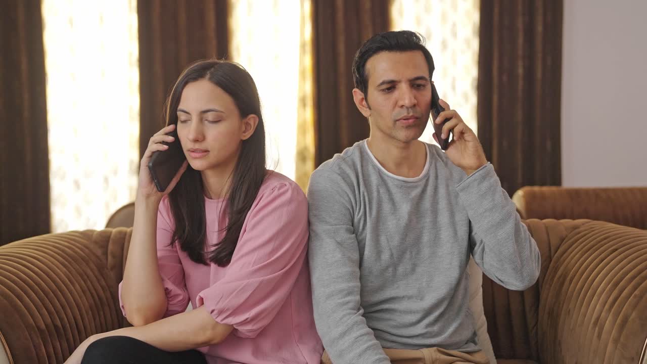 una pareja india hablando en sus teléfonos móviles.