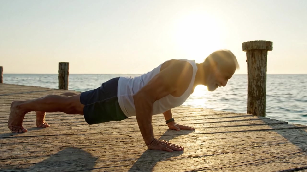 Un anziano attivo dimostra forza ed equilibrio con flessioni su un molo mentre il sole dorato tramonta sulle acque calme, sottolineando il fitness e l'invecchiamento con grazia.